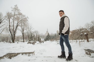 Açık kış portre yakışıklı delikanlı için. Güzel genç onun ceket ve üzerinde bir şehir sokak, köknar ağaçlarının arka plan poz yelek.