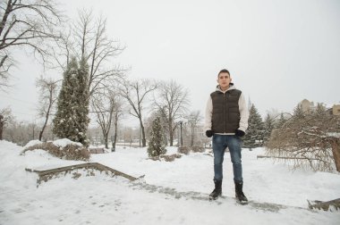 Açık kış portre yakışıklı delikanlı için. Güzel genç onun ceket ve üzerinde bir şehir sokak, köknar ağaçlarının arka plan poz yelek.