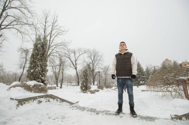 Açık kış portre yakışıklı delikanlı için. Güzel genç onun ceket ve üzerinde bir şehir sokak, köknar ağaçlarının arka plan poz yelek.