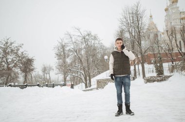 Açık kış portre yakışıklı delikanlı için. Güzel genç onun ceket ve üzerinde bir şehir sokak, köknar ağaçlarının arka plan poz yelek.