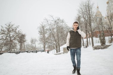 Açık kış portre yakışıklı delikanlı ile belgili tanımlık telefon için. Güzel genç onun ceket ve üzerinde bir şehir sokak, köknar ağaçlarının arka plan poz yelek.