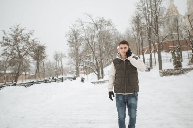 Açık kış portre yakışıklı delikanlı ile belgili tanımlık telefon için. Güzel genç onun ceket ve üzerinde bir şehir sokak, köknar ağaçlarının arka plan poz yelek.