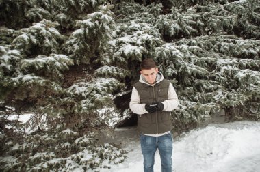 Açık kış portre yakışıklı delikanlı için. Güzel genç onun ceket ve üzerinde bir şehir sokak, köknar ağaçlarının arka plan poz yelek.