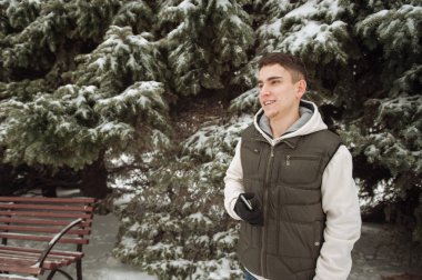 Açık kış portre yakışıklı delikanlı için. Güzel genç onun ceket ve üzerinde bir şehir sokak, köknar ağaçlarının arka plan poz yelek.
