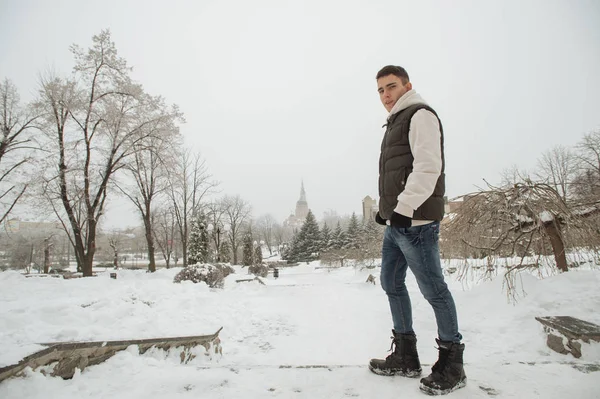 Açık kış portre yakışıklı delikanlı için. Güzel genç onun ceket ve üzerinde bir şehir sokak, köknar ağaçlarının arka plan poz yelek.