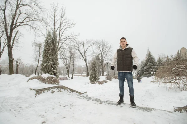 Açık kış portre yakışıklı delikanlı için. Güzel genç onun ceket ve üzerinde bir şehir sokak, köknar ağaçlarının arka plan poz yelek.
