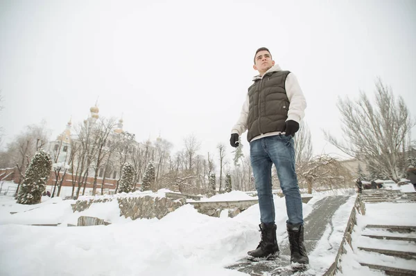 Açık kış portre yakışıklı delikanlı için. Güzel genç onun ceket ve üzerinde bir şehir sokak, köknar ağaçlarının arka plan poz yelek.