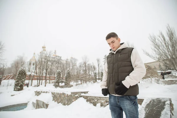 Utomhus vinter porträtt för ung stilig man. Vackra tonåring i hans jacka och väst poserar på en stadsgata, bakgrund av granar. — Stockfoto
