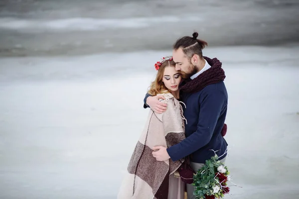 Elegante hermosa pareja joven novia y novio de pie sobre el fondo de un río paisaje de invierno . — Foto de Stock