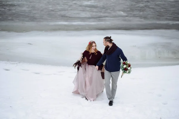 Stilvolle schöne junge Paar Braut und Bräutigam steht auf dem Hintergrund einer Winterlandschaft Fluss. — Stockfoto