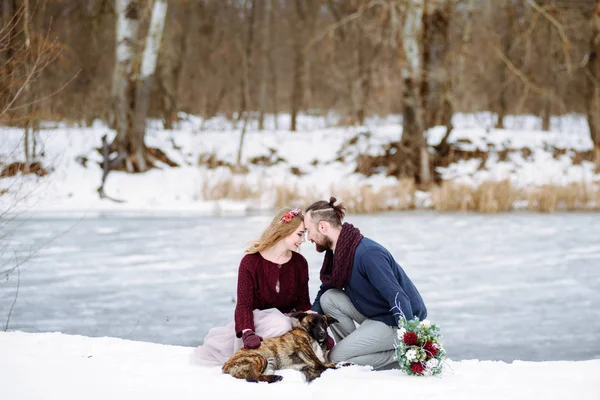 Elegante hermosa pareja joven novia y novio, perro sentado en el fondo de un río paisaje de invierno . —  Fotos de Stock