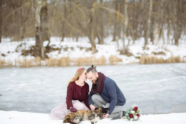 时尚美丽的年轻夫妇新娘和新郎，狗坐在冬季景观河道的背景. — 图库照片