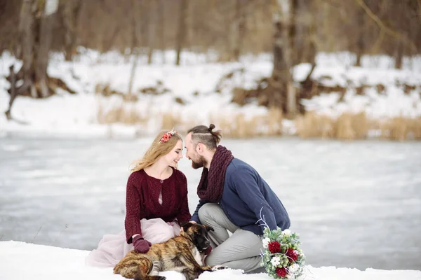 Elegante hermosa pareja joven novia y novio, perro sentado en el fondo de un río paisaje de invierno . — Foto de Stock