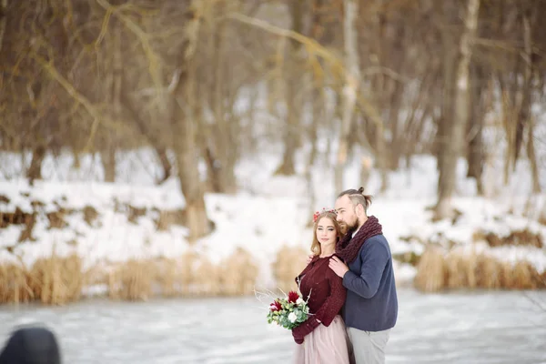 Elegante hermosa pareja joven novia y novio de pie sobre el fondo de un río paisaje de invierno . —  Fotos de Stock