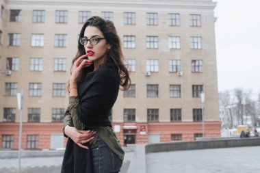 Moda consept: güzel uzun saçlı genç kız gözlük, yeşil takım ve gri kot modern duvarının yakınında duran kırmızı dudaklar. Evet istedi. 