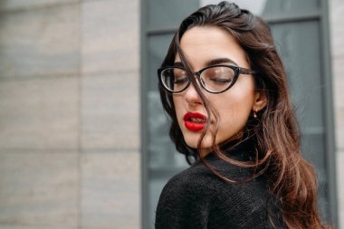 Moda consept: güzel uzun saçlı genç kız gözlük, yeşil takım ve gri kot modern duvarının yakınında duran kırmızı dudaklar. Evet istedi. 