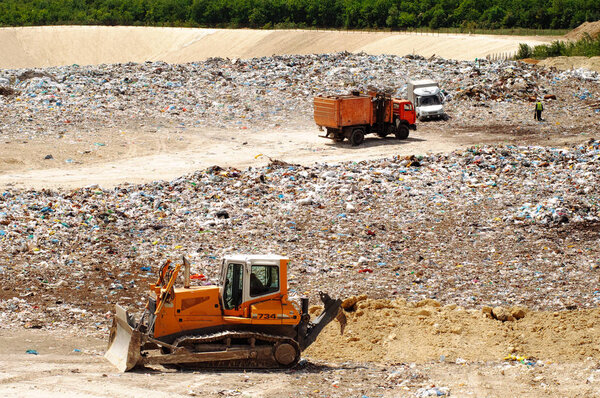 Truck working in landfill with birds looking for food. Garbage on the city dump. Soil pollution. Environmental protection.