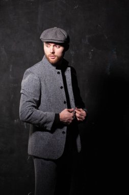 Serious handsome young bearded man in hat on grey background looking at side. Portrait of man against grey wall.