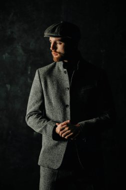 Serious handsome young bearded man in hat on grey background looking at side. Portrait of man against grey wall.