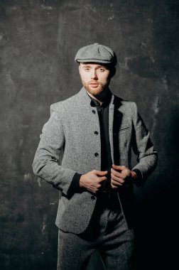 Ready for business. A bearded man in a cap and a gray suit fastens his jacket.