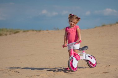 Kırsalda bisiklet yolunda dengeli bisiklete binen küçük bir kız.  