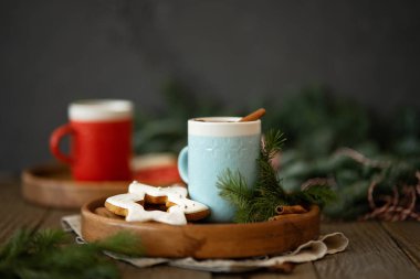 Seramik bardakta sıcak bir içecek ve taze köknar dallarıyla çevrili ahşap tepside zencefilli ekmek.