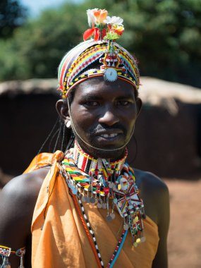 Kenya 'da gülümseyen bir Masai savaşçısının portresi geleneksel boncuklu mücevherler takıyor ve çiçeklerle süslenmiş eşsiz bir başlık takıyor. Otantik Afrika kabile kültürü.