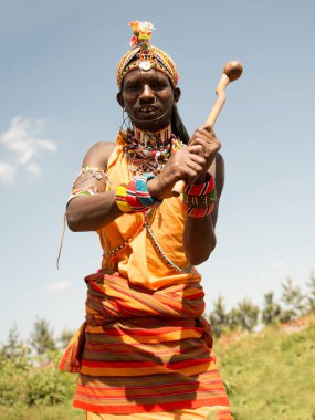 Kenya 'da gülümseyen bir Masai savaşçısının portresi geleneksel boncuklu mücevherler takıyor ve çiçeklerle süslenmiş eşsiz bir başlık takıyor. Otantik Afrika kabile kültürü.