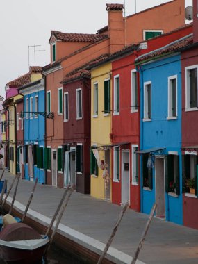 Venedik, Burano adasında canlı, düz, parlak bir sıra ev mavisi, sarı, kırmızı ve orangutan. Açık gün ışığı renkli cepheleri ve terasotta çatılarını vurguluyor.