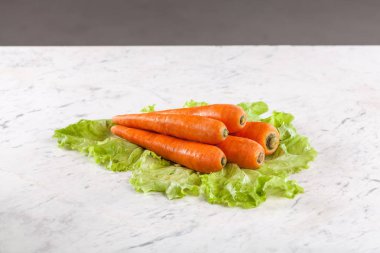 Beyaz mermer bir masada yeşil marul yaprakları üzerinde taze çiğ turuncu havuçlar. Salata veya diyet gıda konsepti için organik sağlıklı sebze malzemeleri.
