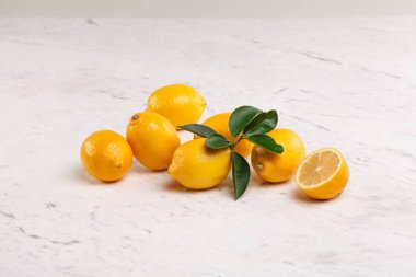 Bir grup taze sarı limon ve beyaz mermer arka planda yeşil narenciye yapraklı yarım limon. Parlak ve ekşi narenciye bileşimi C vitamini bakımından zengin..