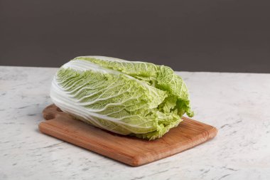 Napa 'nın lahana kafası beyaz mermer bir masada tahta bir kesme tahtasının üzerinde. Çiğ organik Çin lahanası ve kırışık yeşil yapraklar. Salata veya kimçi pişirmek için sağlıklı sebze malzemesi hazır..