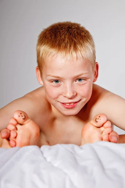 Мальчик в постели с улыбающимися лицами на пальцах ног — стоковое фото