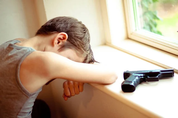 Niño descansando en el alféizar de la ventana con una pistola cerca de él — Foto de Stock