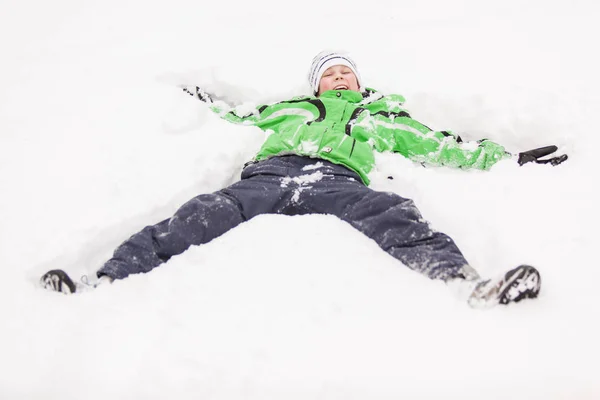 Młody chłopak gra w śniegu leżącego na plecach — Zdjęcie stockowe