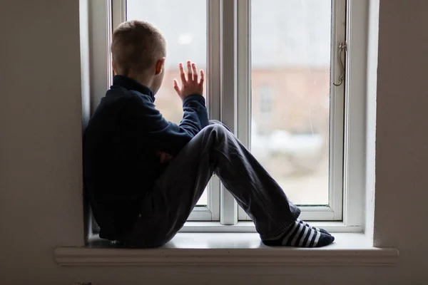 Young boy sitting on a windowsill waving — Stock Photo, Image