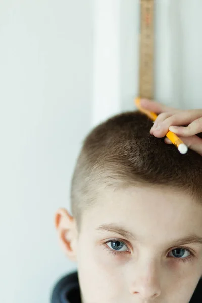 Мальчик держит карандаш на голове, чтобы проверить высоту — стоковое фото