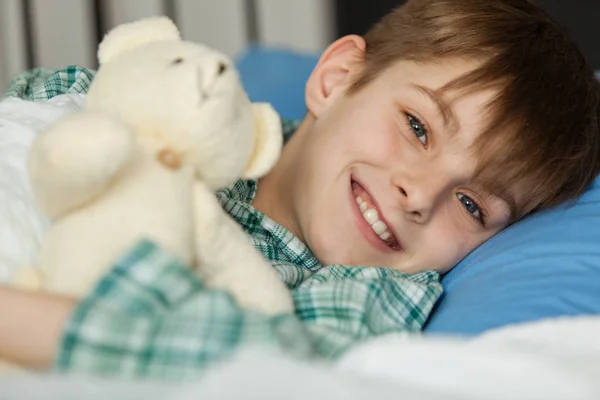 Rapaz feliz com seu ursinho de pelúcia deitado em sua cama — Fotografia de Stock