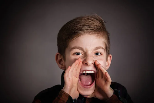 Rapaz bonito gritando com a câmera contra cinza — Fotografia de Stock