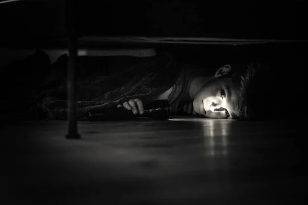Trauriger kleiner Junge mit Taschenlampe liegt unter seinem Bett — Stockfoto