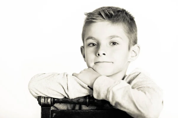Netter Junge lehnt auf einem Stuhl in monochromer Farbe — Stockfoto