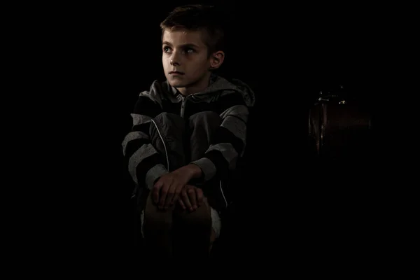 Seated Thoughtful Boy sostiene sus pies contra el negro — Foto de Stock