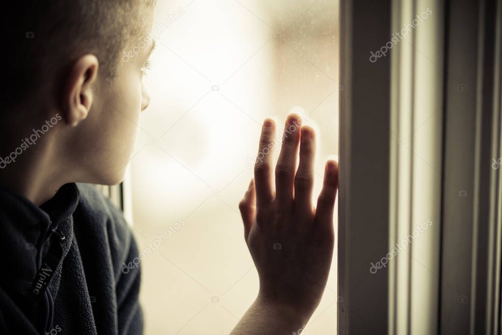 Sad Boy Looking Outside While Holding Glass Window