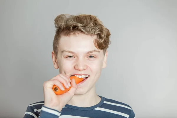 Веселый мальчик, кусающий свежую морковку. — стоковое фото