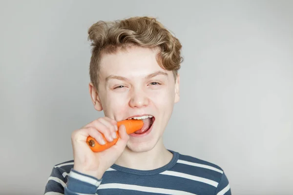 Young teenage boy biting a fresh raw carrot