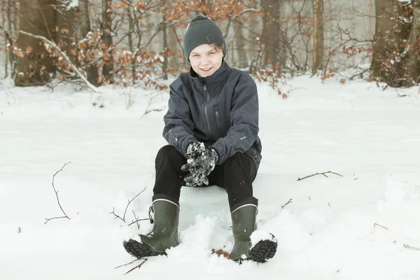 Uśmiechnięty, Nastolatka siedzi w śniegu w pobliżu lasu — Zdjęcie stockowe