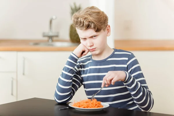 Pouting boy sitting in front of shredded carrots — Stock Photo, Image