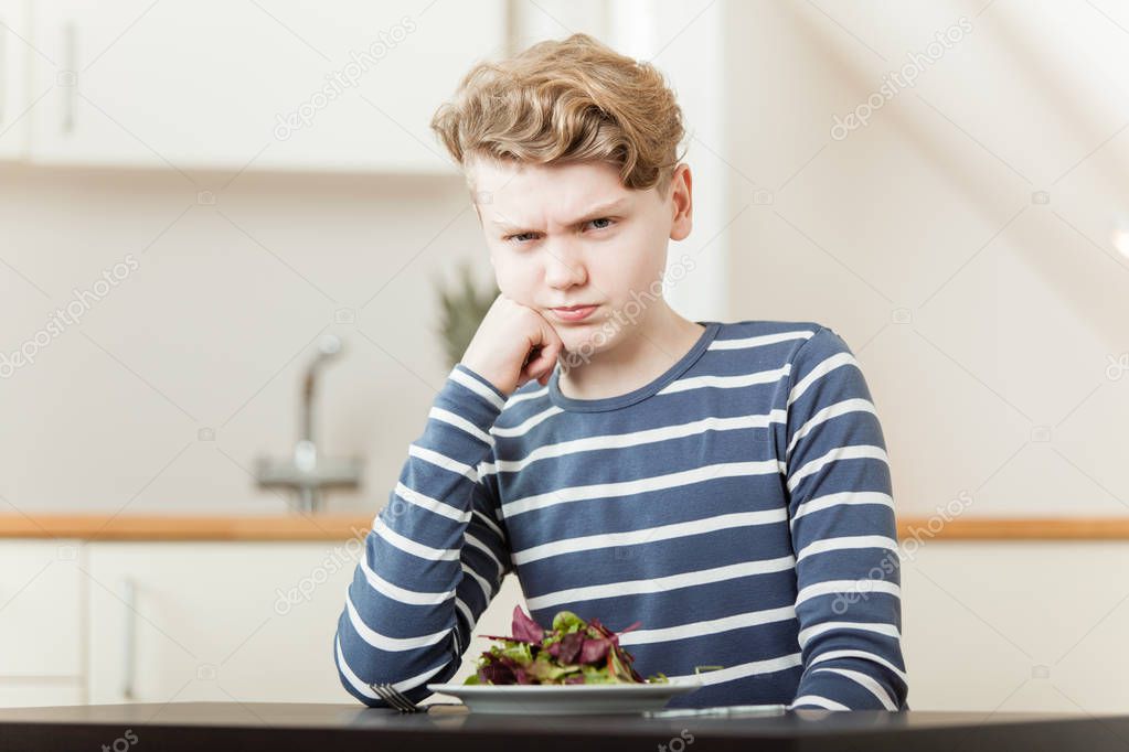 Pouting boy sitting in front of salad greens