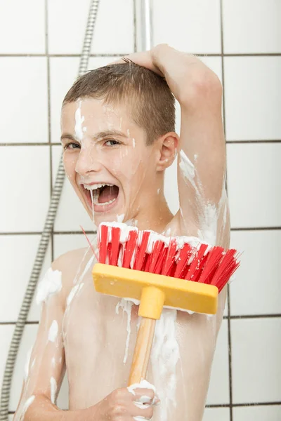 Young boy with broom brush in the shower — Stockfoto