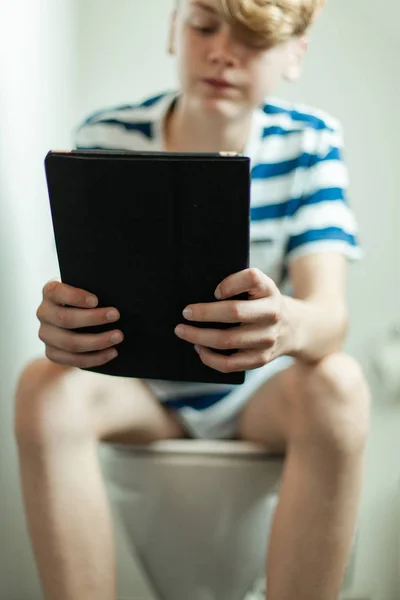Ragazzo adolescente che legge un tablet sul water — Foto Stock